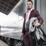 Smart Luggage - Serious stylish bearded businessman in trendy suit holding bag and coat in hands standing near train on platform in railway station and looking away