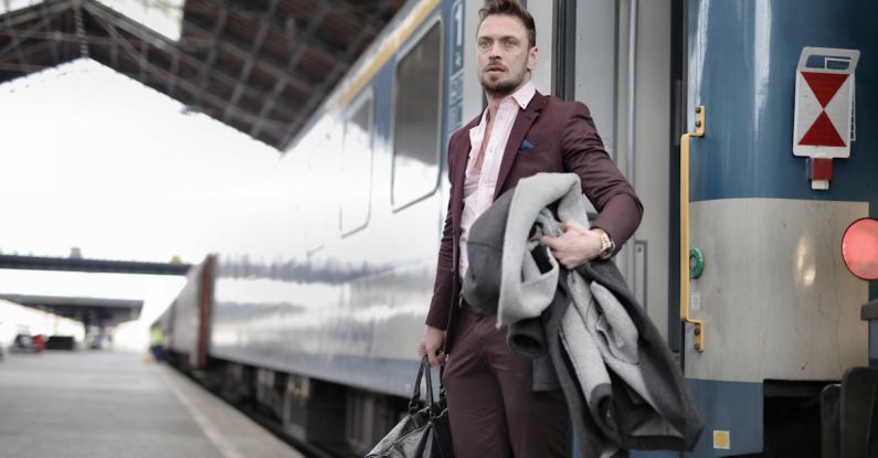 Smart Luggage - Serious stylish bearded businessman in trendy suit holding bag and coat in hands standing near train on platform in railway station and looking away
