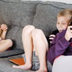 Habit Tracking Apps - Positive barefoot children in casual wear resting together on cozy couch and browsing tablets and smartphones