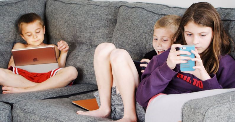 Habit Tracking Apps - Positive barefoot children in casual wear resting together on cozy couch and browsing tablets and smartphones