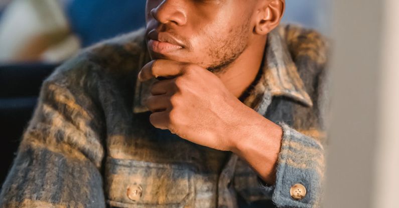 Digital Mindfulness - Serious young African American male freelancer thoughtfully looking away and touching chin while working on computer