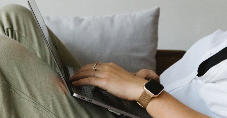 Smart Home Hub - Side view of crop unrecognizable female freelancer in casual clothes and smartwatch lying on comfortable sofa and working remotely on laptop