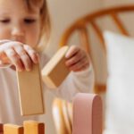 Educational Games - Cute little girl in white casual clothes standing near table and playing with wooden blocks while spending time at home
