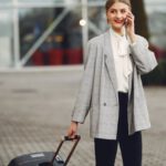 Smart Suitcases - Stylish businesswoman speaking on smartphone while standing with luggage near airport